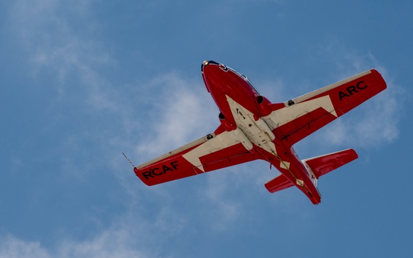 Three red and white military jet aircraft are photographed from below in tight formation flight against a partly cloudy blue sky. The aircraft bear markings 'RCAF' (Royal Canadian Air Force) on their wings and 'ARC' (Armée de l'air du Canada, the French equivalent) on the opposite wings. This appears to be a performance by the Canadian Forces Snowbirds aerobatic demonstration team flying CT-114 Tutor jets.