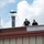 Two law enforcement officers are positioned on a rooftop, appearing to conduct surveillance or a security sweep. One officer wears a vest labeled 'Border Patrol' and the other wears a vest labeled 'Police HSI' (Homeland Security Investigations). The scene suggests a coordinated federal law enforcement operation.