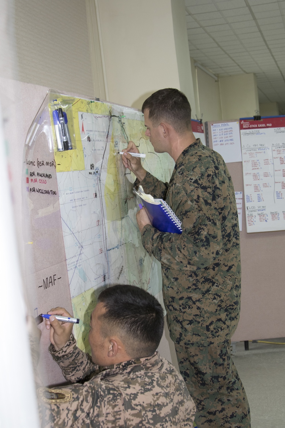 U.S. Marine Cpl. Thomas Richards, works with Mongolian Armed Forces Capt. BatsukhTseenorov to mark troop locations in the lower control operations cente.