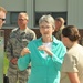 A civilian woman in a teal blouse is engaged in conversation with military personnel outdoors near a building. She appears to be speaking with a female soldier in tan/multicam uniform while other Air Force and Army personnel stand nearby. The setting appears to be a military installation or base.