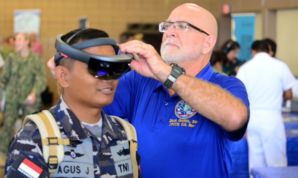 Mark Griffith, Joint Tele-Critical Care Network, fits a Republic of Indonesia sailor with a virtual reality headset during the RIMPAC 2018 Inaugural Innovation Fair