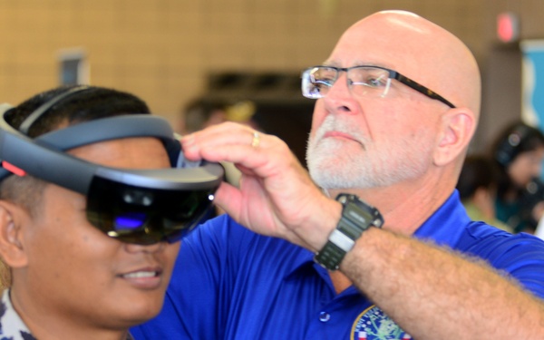 Mark Griffith, Joint Tele-Critical Care Network, fits a Republic of Indonesia sailor with a virtual reality headset during the RIMPAC 2018 Inaugural Innovation Fair