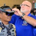 Mark Griffith, Joint Tele-Critical Care Network, fits a Republic of Indonesia sailor with a virtual reality headset during the RIMPAC 2018 Inaugural Innovation Fair