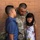 A U.S. Army soldier in OCP (Operational Camouflage Pattern) uniform embraces two children, likely his son and daughter, against a brick wall background. The soldier's name tape partially reads 'LLANEZ' and rank insignia is visible on the uniform. The scene appears to be a family reunion or farewell moment.