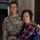 A U.S. Army soldier named Nguyen, wearing OCP (Operational Camouflage Pattern) uniform, poses with an older woman who appears emotional, likely a family member. The soldier has a Staff Sergeant rank insignia visible on his uniform. The setting appears to be an indoor venue, possibly during a military ceremony or graduation event.