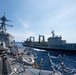 Two naval vessels are conducting an underway replenishment (UNREP) operation at sea, with transfer lines visibly connecting the two ships. The vessel on the right bears the hull number '304' with the prefix 'OR', indicating a replenishment or auxiliary ship. The ship on the left appears to be a guided-missile destroyer based on its superstructure, radar arrays, and deck-mounted weapons systems.