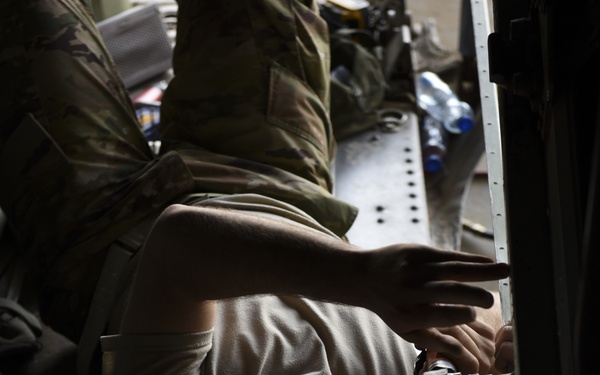 The image shows military personnel in camouflage uniforms performing maintenance or repair work on what appears to be a large military aircraft, likely working on an interior panel or structural component. The photo is rotated 90 degrees, making the subjects appear sideways. At least two individuals are visible using hand tools, with one wearing safety glasses.