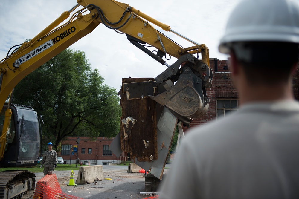 Airmen help guide heavy equipment operator as they restore buildings at the West Virginia Schools for the Deaf and the Blind