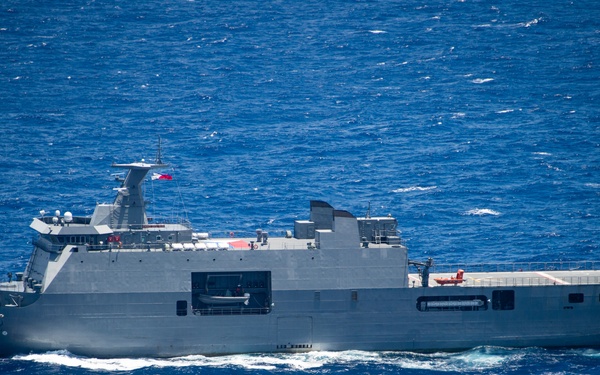 A large gray military amphibious assault or landing ship is underway on open blue ocean waters. The vessel is flying what appears to be a Philippine flag from its mast, suggesting it belongs to the Philippine Navy. The ship features a flat deck, a well deck opening on the hull side, and a superstructure with radar and communications equipment.