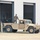 A military HMMWV (Humvee) in desert tan coloring is parked in front of a metal warehouse-style building with multiple large bay doors. One soldier in camouflage uniform is standing in the cargo bed of the vehicle, while other personnel are visible in the background near the open bays. The setting appears to be a military installation or motor pool area.