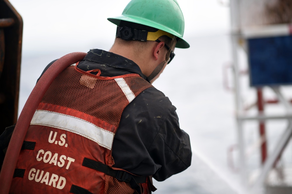 A Coast Guard Cutter Fir crewmember power-washes marine growth off the bottom of a whistle buoy in Panama