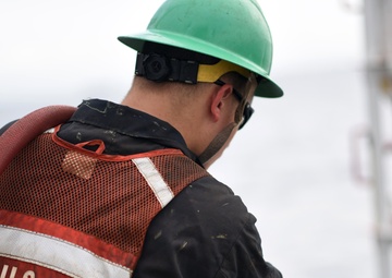 A Coast Guard Cutter Fir crewmember power-washes marine growth off the bottom of a whistle buoy in Panama