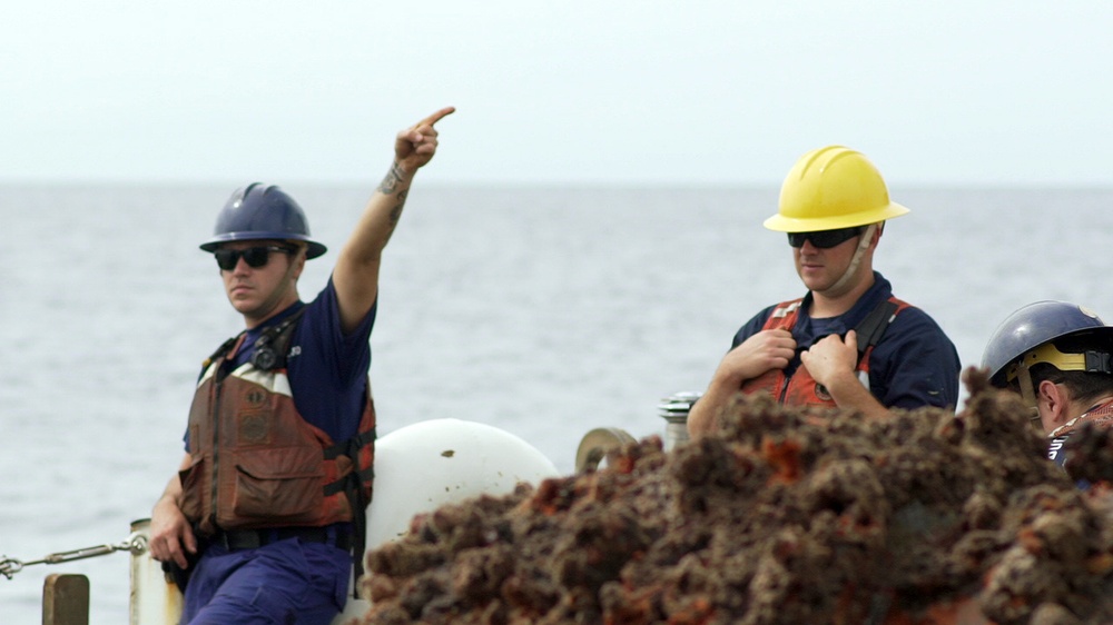 A Coast Guard Cutter Fir deck supervisor gives a signal to the crane operator