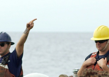 A Coast Guard Cutter Fir deck supervisor gives a signal to the crane operator
