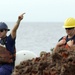 A Coast Guard Cutter Fir deck supervisor gives a signal to the crane operator