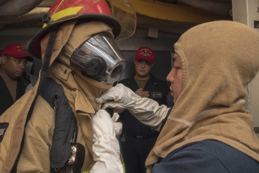 Culinary Specialist 2nd Class Allyson Gonzales (right), from San Diego, assists a Sailor dressing out in firefighting gear on the Ticonderoga-class guided-missile cruiser USS Antietam (CG 54) during a general quarters training exercise