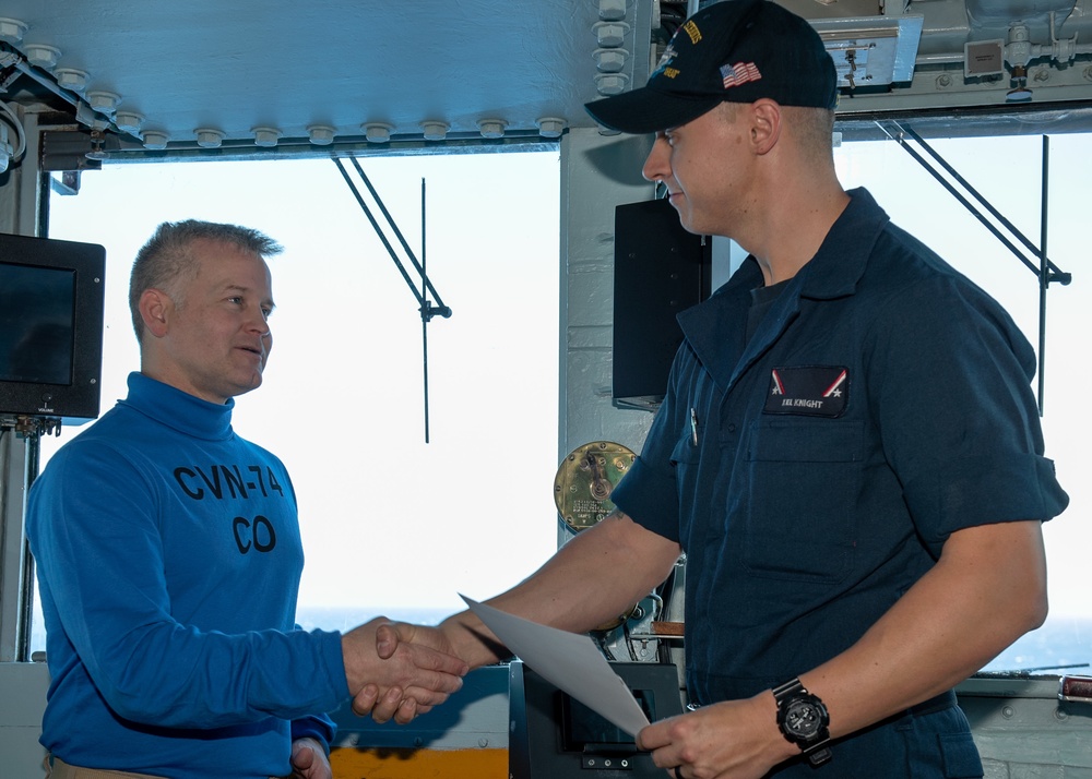 Fireman Kiel Knight, right, from Panama City, Florida, receives a Commanding Officer’s coin from Capt. Randy Peck, commanding officer of the Nimitz-class Aircraft Carrier USS John C. Stennis (CVN 74), as the Sailor of the Day.