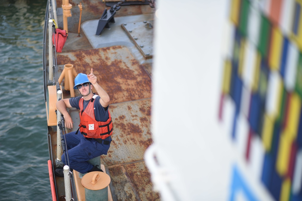 Seaman Joseph Griffin points to the Coast Guard Tahoma's bridge as the vessel sets sail for UNITAS 2018