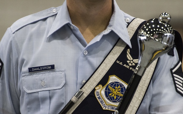 A U.S. Air Force senior non-commissioned officer named Dahlstrom is shown in dress uniform holding a ceremonial mace. The individual is wearing a decorative sash bearing the 'Air Mobility Command' patch and 'U.S. Air Force' insignia, along with white ceremonial gloves. This appears to be a formal military band or honor guard ceremony.