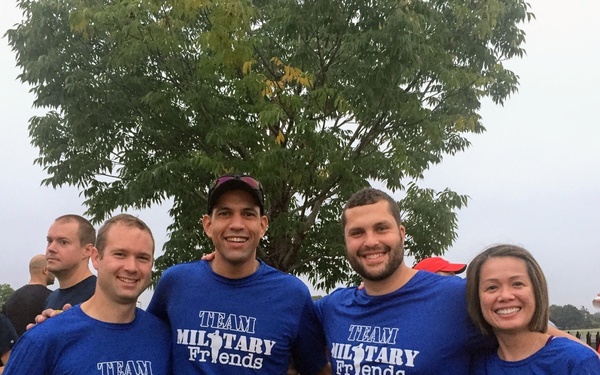 Four runners wearing matching blue 'Team Military Friends' t-shirts pose together at what appears to be the Army Ten-Miler race event. They are displaying race bibs with numbers visible including 2391, 2852, 8075, and 22494. The group appears to be in good spirits, smiling and giving thumbs up, likely before or after the race.