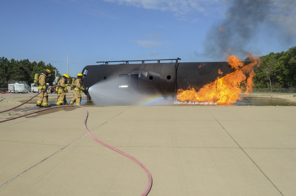 Firefighters with the 128th Air Refeuling Wing spray water at a mock aircraft trainer to extinguish a fire during their annual training at Volk Field Combat Readiness Training Center