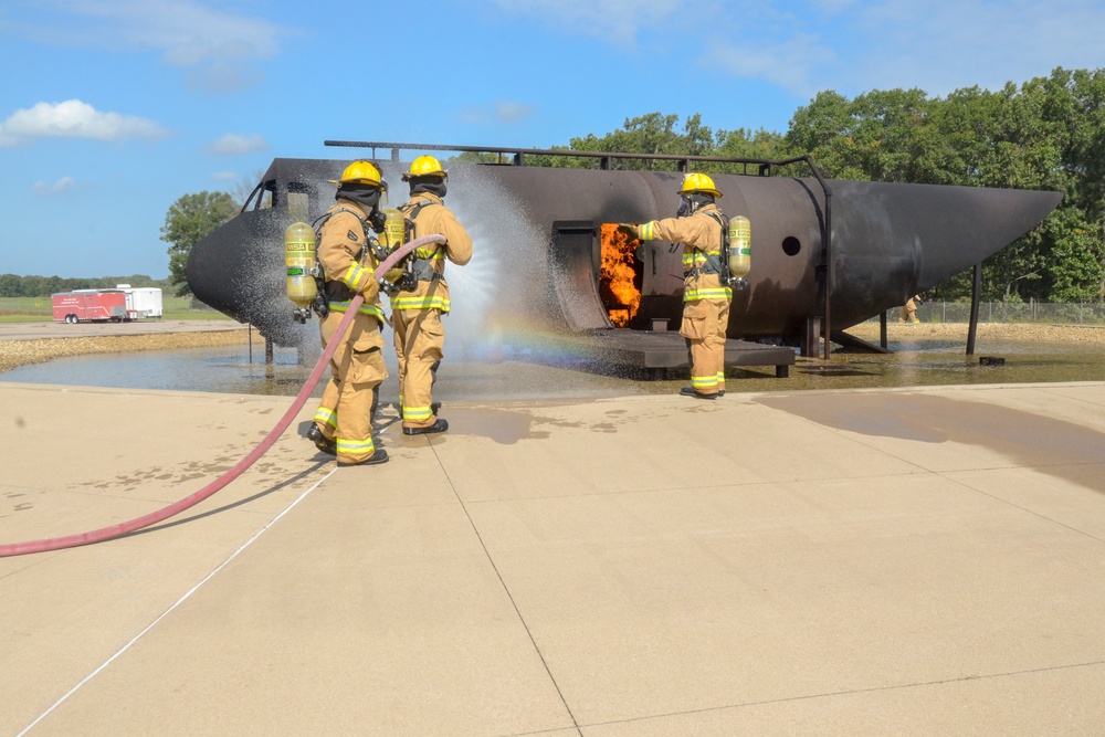 Firefighters with the 128th Air Refeuling Wing spray water at a structural trainer to extinguish a fire during their annual training at Volk Field Combat Readiness Training Center