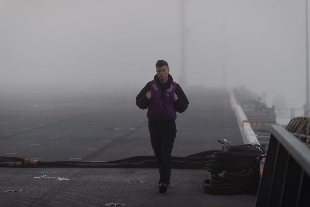 Sailor traverses the flight deck in fog