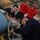 First test bombs dropped from HMS Queen Elizabeth’s F-35 Lightning fighter jets Four military personnel are working in what appears to be an aircraft hangar, with two individuals actively handling ordnance or a weapons system mounted on an aircraft. Two observers wearing red 'VX-23' sweatshirts watch the procedure, suggesting a training or evaluation context. The unit designation 'VX-23' refers to a U.S. Navy test and evaluation squadron.