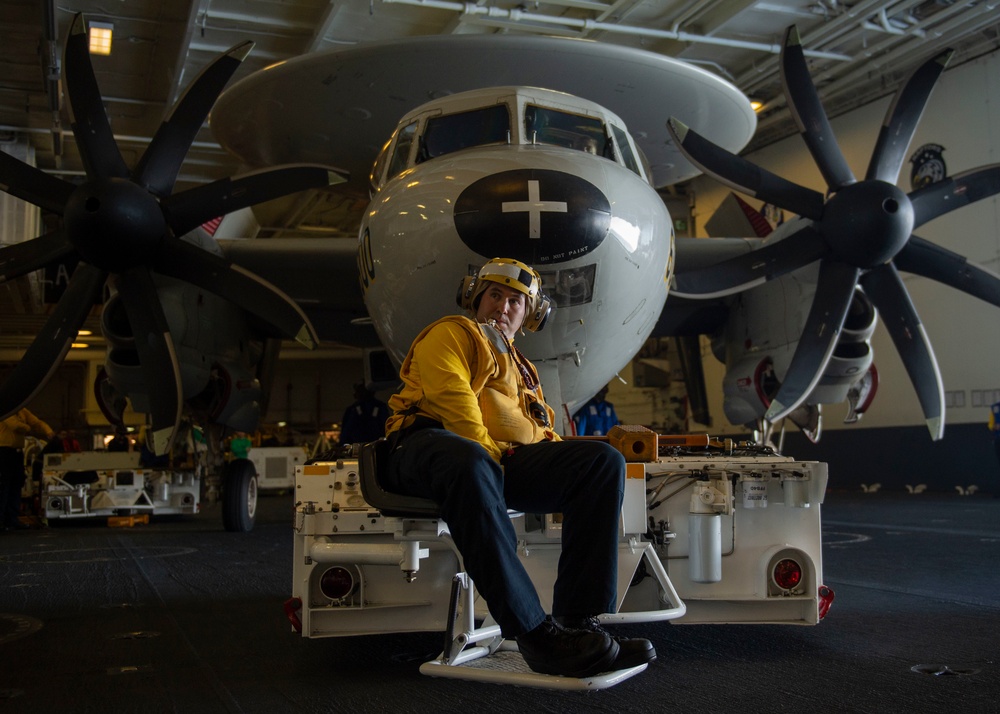 Aviation Boatswain’s Mate (Handling) 2nd Class Justin Hill, from Bakersfield, California, maneuvers an E-2C Hawkeye, with Electronic Attack Squadron (VAQ) 133, in the hangar bay aboard the Nimitz-class aircraft carrier USS John C. Stennis (CVN 74).