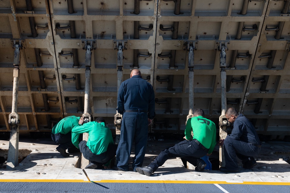 Sailors conduct maintenance on a jet blast deflector on the flight deck aboard the Nimitz-class aircraft carrier USS John C. Stennis (CVN 74).