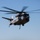 A large military heavy-lift helicopter, identifiable as a Sikorsky CH-53E Super Stallion, is captured in flight against a clear blue sky. The aircraft bears the number '04' on its fuselage and displays military markings consistent with U.S. Marine Corps livery. A cargo hook and sling line are visibly deployed beneath the aircraft, suggesting a heavy-lift or external load operation.