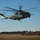 A large military helicopter marked '04' with 'MARINES' visible on the fuselage is hovering at low altitude over an open field. The aircraft appears to be a Sikorsky CH-53E Super Stallion operated by the United States Marine Corps. A control tower and radar dome are visible in the background, indicating a military airfield setting.