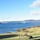 A large-scale military exercise is underway in what appears to be a Scandinavian fjord setting, likely Norway. Multiple military assets are simultaneously visible including ground vehicles, helicopters, naval vessels, and fixed-wing aircraft. The coordinated multi-domain operation suggests a NATO or allied forces joint exercise.