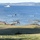 A large-scale military exercise is underway in what appears to be a Scandinavian coastal setting, likely Norway. Two large military helicopters, identifiable as CH-53E Super Stallions with U.S. Marine Corps markings, fly low over green fields while ground vehicles including tanks and armored personnel carriers are positioned below. Multiple naval vessels, including a large warship, are visible in the fjord in the background.