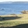 The image depicts a military amphibious landing exercise taking place along a fjord coastline, likely in Norway based on the landscape characteristics. Ground troops and armored vehicles are advancing across open fields while multiple landing craft approach the shore from the water. Two larger naval vessels are visible in the background on the fjord.