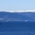 A formation of multiple gray naval vessels is transiting a wide fjord or strait with snow-capped mountains and forested hillsides visible in the background. The largest vessel is prominently positioned in the foreground left, with at least four additional warships spread across the middle distance. The scene suggests a multinational naval exercise or fleet transit in a Nordic or Scandinavian waterway.