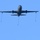 A military tanker aircraft is photographed from below against a clear blue sky, with three refueling hoses and drogues visibly deployed and trailing downward. The aircraft appears to be in a hose-and-drogue aerial refueling configuration, with one centerline drogue and two wing-mounted drogues extended. The dark gray paint scheme and configuration are consistent with a military aerial refueling tanker.