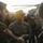 A multinational military gathering showing personnel from at least three nations interacting near a helicopter. A U.S. Marine (name tape reads 'NEGRON') in MARPAT digital camouflage is shaking hands and smiling with soldiers wearing German Bundeswehr flecktarn uniforms. A French soldier with a tricolor flag patch is visible in the background, suggesting a NATO or coalition exercise or meeting.