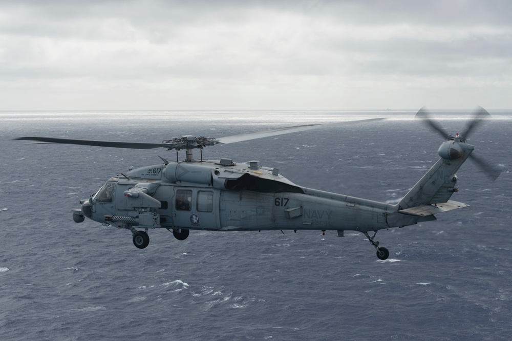 An MH-60S Knight Hawk, with Helicopter Sea Combat Squadron (HSC) 14, flies toward the Nimitz-class aircraft carrier USS John C. Stennis (CVN 74).