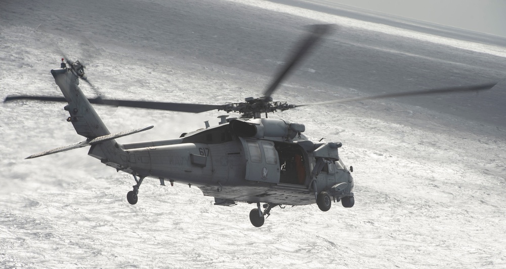 An MH-60S Knight Hawk, with Helicopter Sea Combat Squadron (HSC) 14, flies towards the Nimitz-class aircraft carrier USS John C. Stennis (CVN 74).