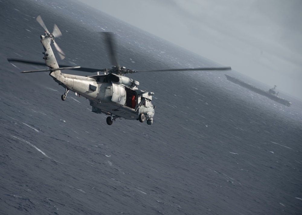 An MH-60S Knight Hawk, with Helicopter Sea Combat Squadron (HSC) 14, flies towards the Nimitz-class aircraft carrier USS John C. Stennis (CVN 74).