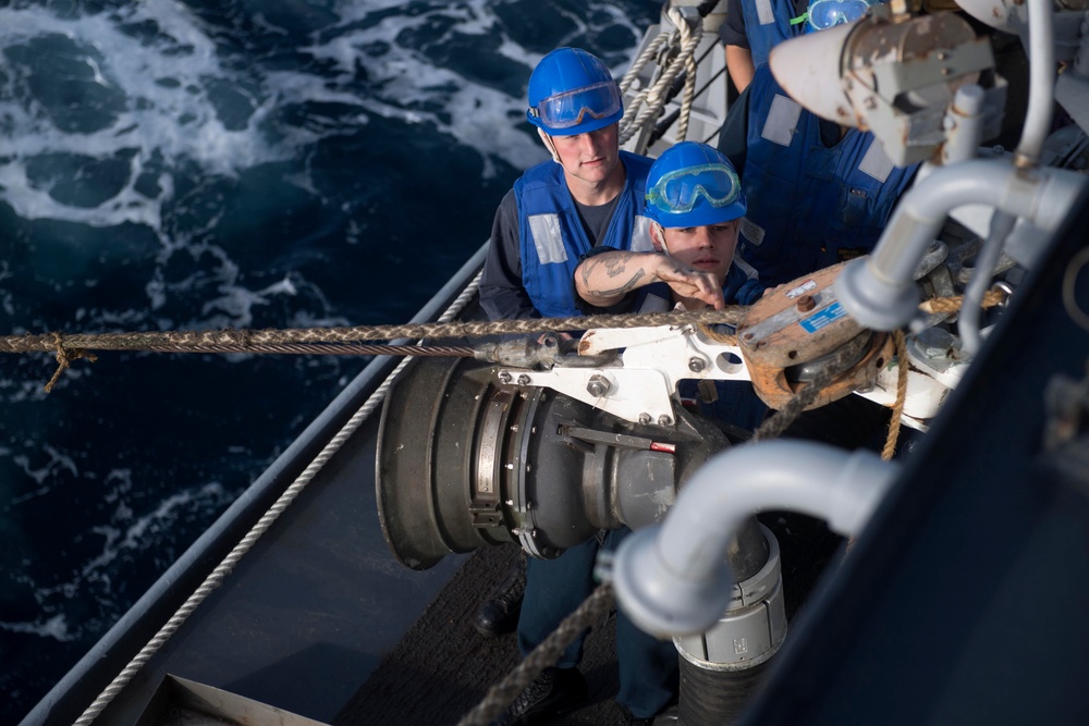 Boatswains Mate 3rd Class Brandon Ross, from Honeapath, South Carolina, observes Seaman Andrew Simpson, from Lafayette, Tennessee, as he cuts stoppers on the span wire at a fuel station aboard USS Spruance (DDG 111) during a replenishment-at-sea.