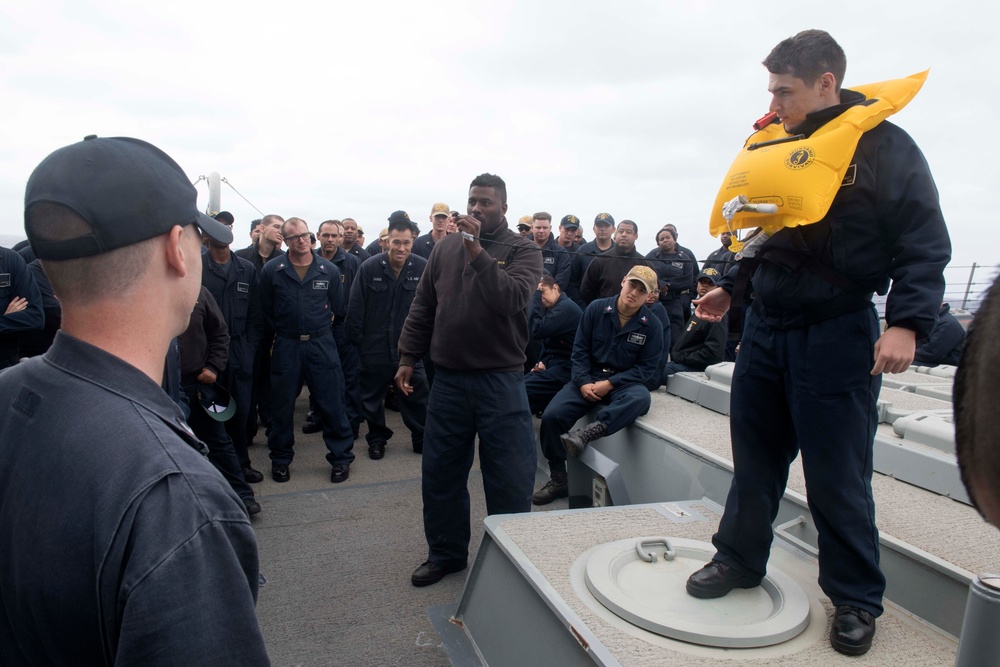 Boatswain’s Mate 3rd Class Mark Sturge, center, from Fredericksburg, Virginia, uses Operations Specialist Seaman Kevin Kennedy, from Perth Amboy, New Jersey, to demonstrate abandon ship training aboard USS Spruance (DDG 111).