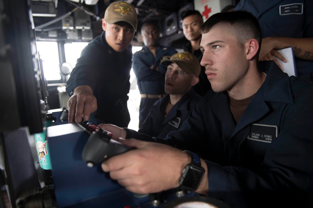 Gunner’s Mate Seaman Dylan King, right, operates the remote operation console (ROC) of a Mark 38 25 mm machine gun system while receiving training from Gunner’s Mate 2nd Class Brandon Diep, left, in the pilot house aboard USS Spruance (DDG 111).