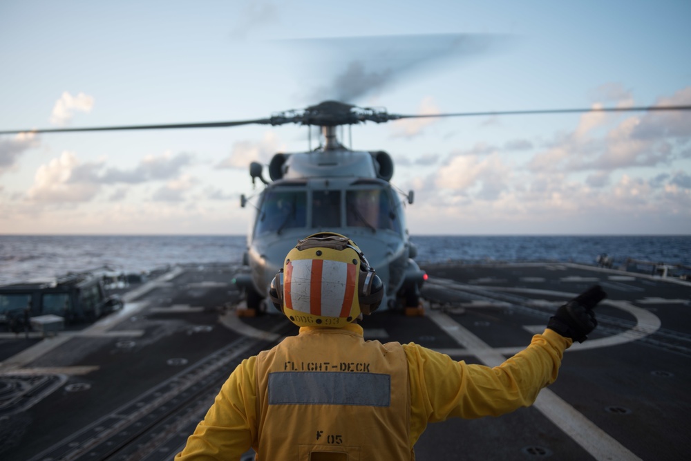 Boatswain’s Mate 2nd Class Melvin Bergado, assigned to USS Chung-Hoon (DDG 93), signals to the pilots of an MH-60R Sea Hawk.