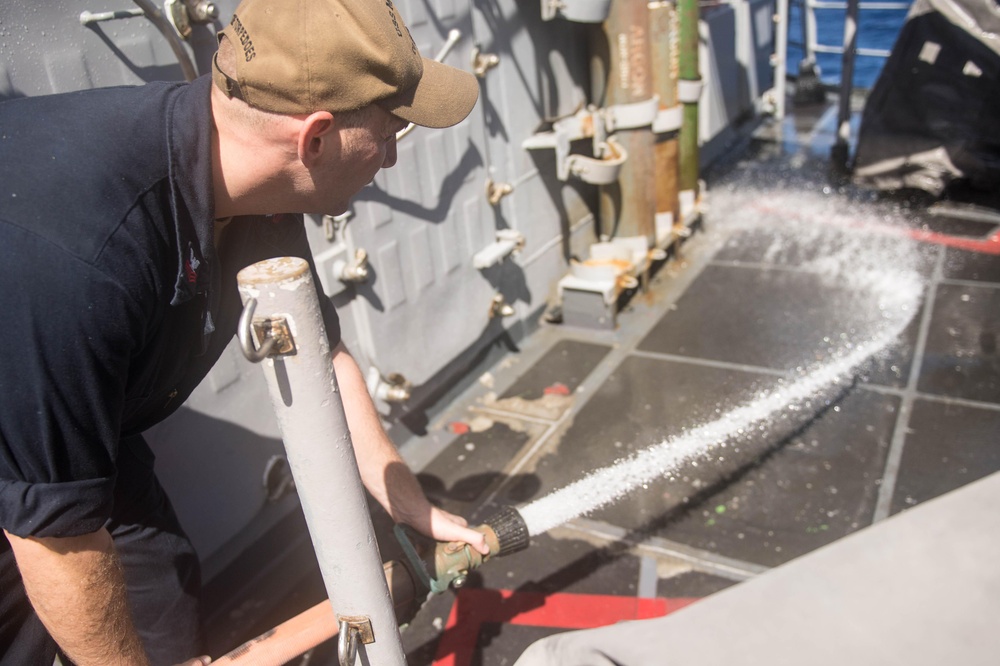 Fire Controlman (Ageis) 1st Class William Long sprays water on the deck of USS Mobile Bay (CG 53) during a fresh-water washdown.