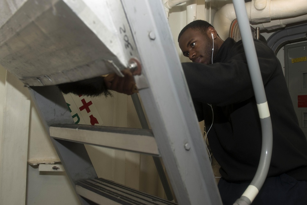 Information Systems Technician 3rd Class Marshon Wade dusts a ladderwell during cleaning stations aboard USS Spruance (DDG 111).