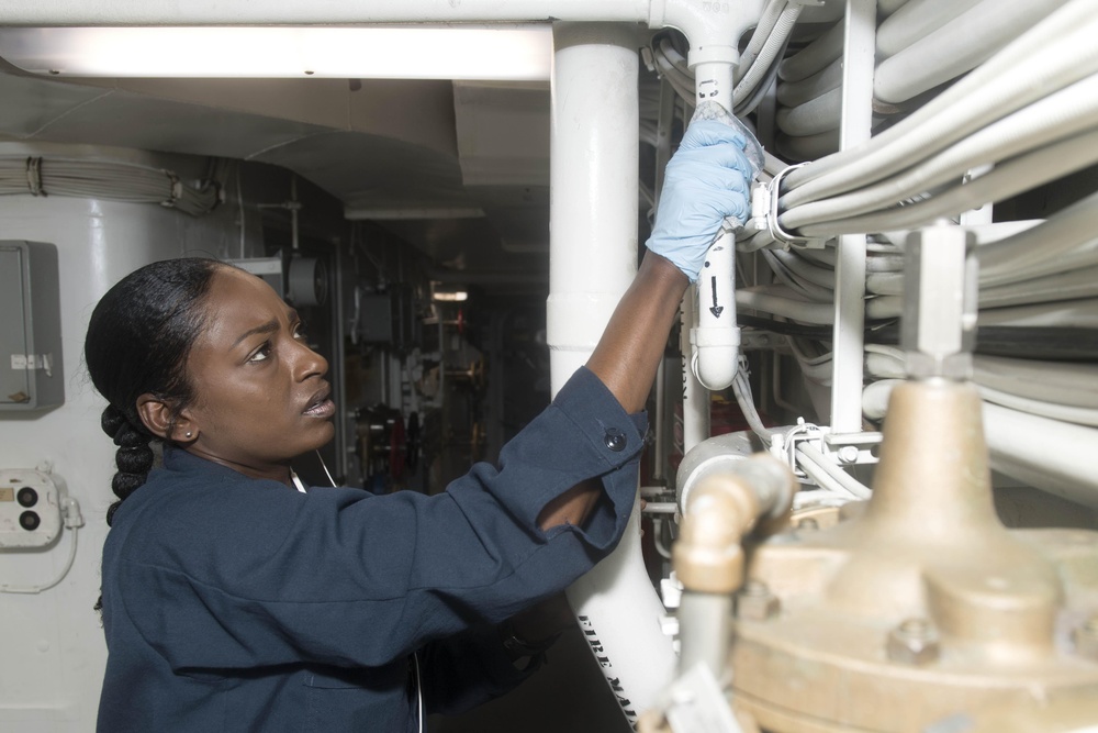 Logistics Specialist 2nd Class Nakosha Embry wipes down pipes and wires during cleaning stations aboard USS Spruance (DDG 111).