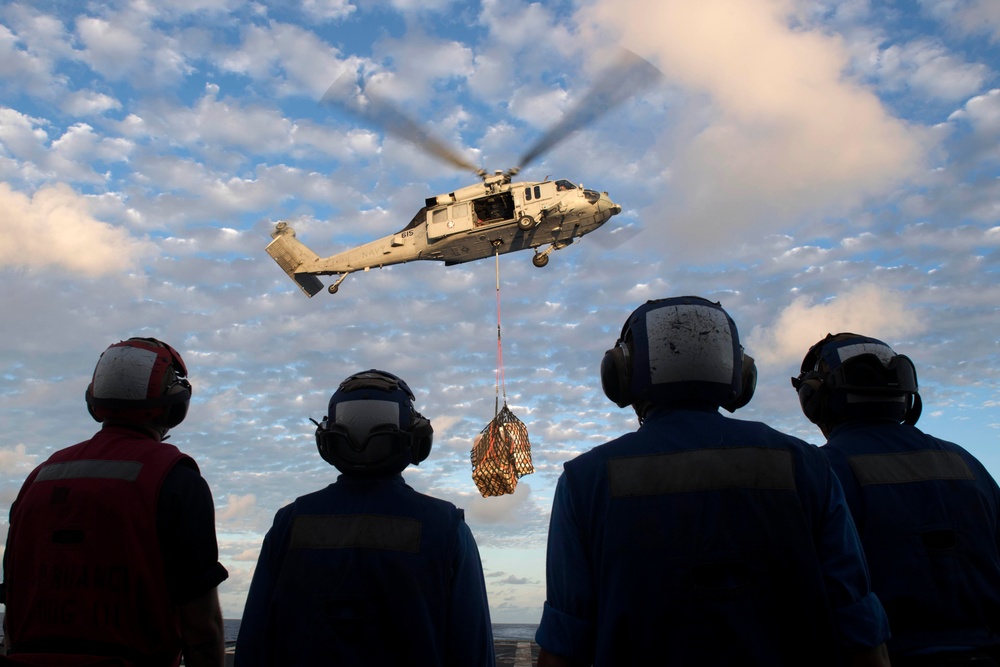 Sailors wait to retrieve cargo as an MH-60S Sea Haw lowers supplies onto the flight deck of USS Spruance (DDG 111) during a vertical replenishment.