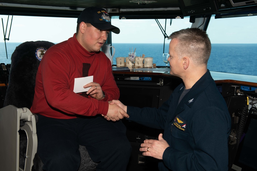 Aviation Ordnanceman 3rd Class Dylan Drake receives a coin for his selection as the USS John C. Stennis (CVN 74) Sailor of the Day from Capt. Randy Peck, commanding officer of John C. Stennis.